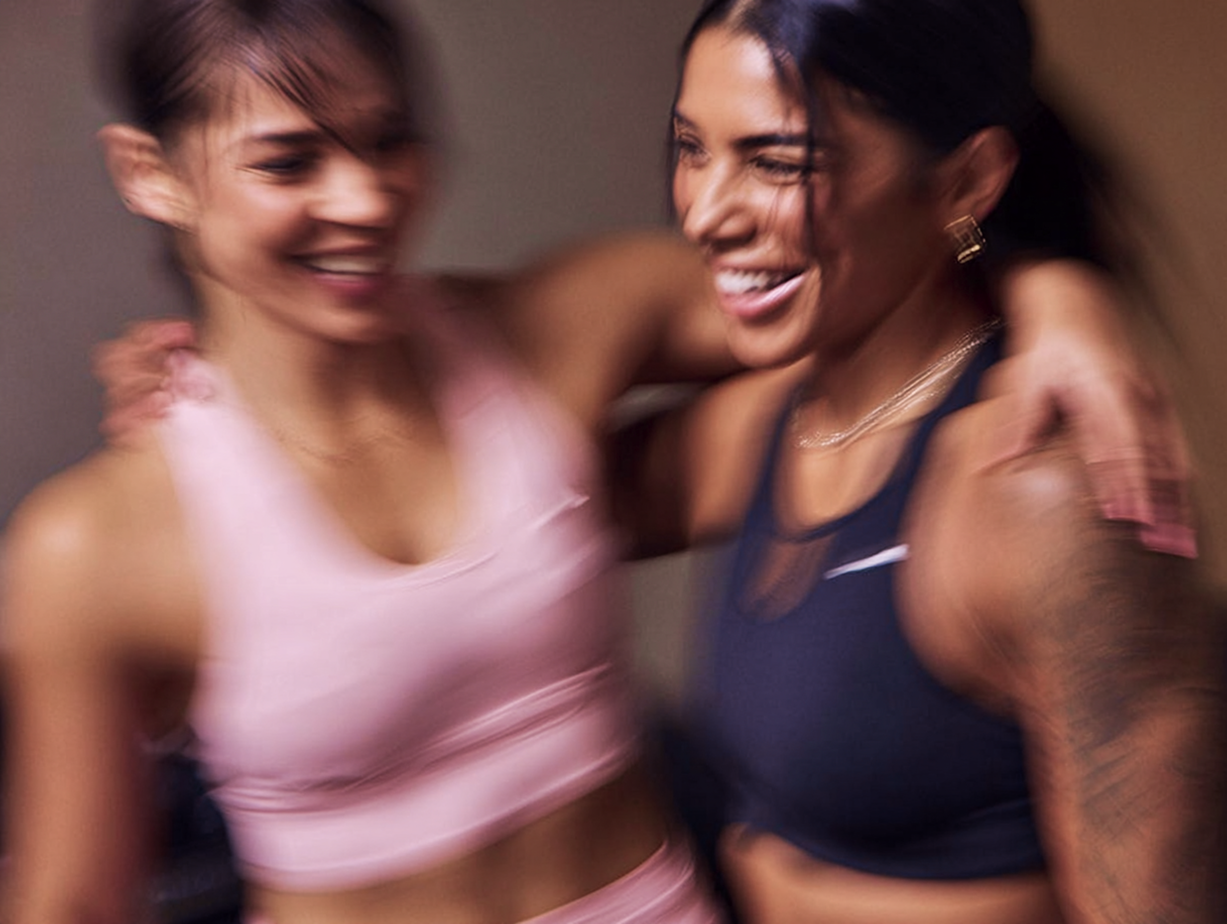 Zwei Frauen in Sportkleidung umarmen sich und zeigen ihre Freundschaft und Energie in einer sanft verschwommenen Umgebung.
